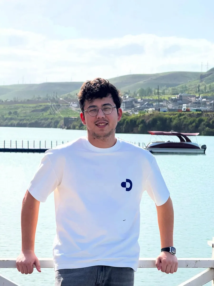 Yusuf smiling by a lake, in a white t-shirt